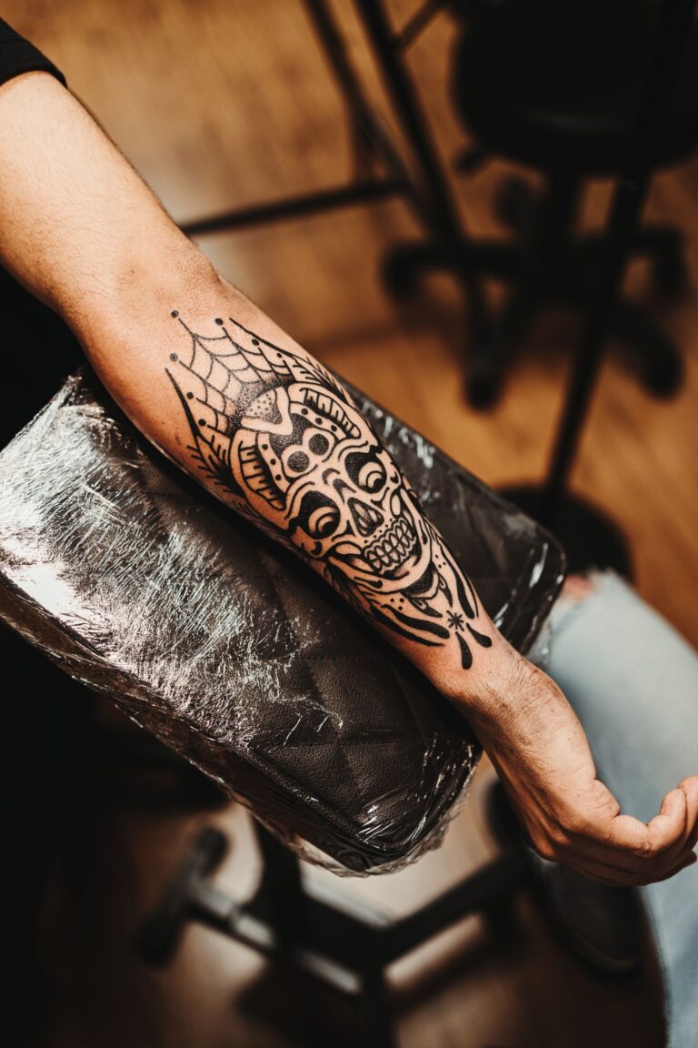 Close-up of a detailed skull tattoo on a man's forearm in a tattoo studio setting.