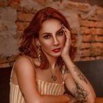 Portrait of a woman with tattoos and red hair in a modern indoor setting. and Portrait of a woman with tattoos and red hair in a modern indoor setting.