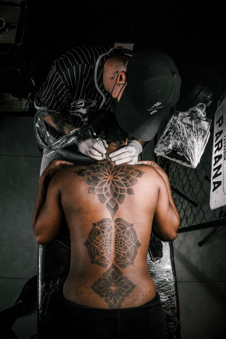 Tattoo artist working on a large geometric back tattoo in a studio setting.